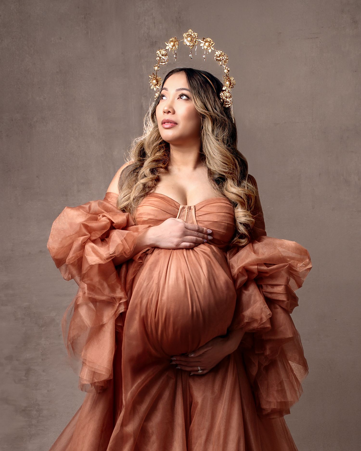 Close-up pregnancy portrait woman wears an ornate gold halo crown with flowers and little stars hanging down.