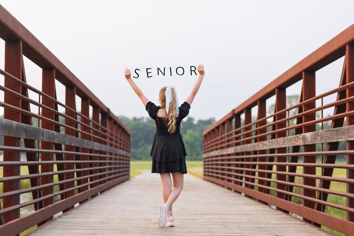 Female teen, back to the camera, holding a sign over her head that reads: "SENIOR." Senior pictures by MegMc Photography, Medina, TN
