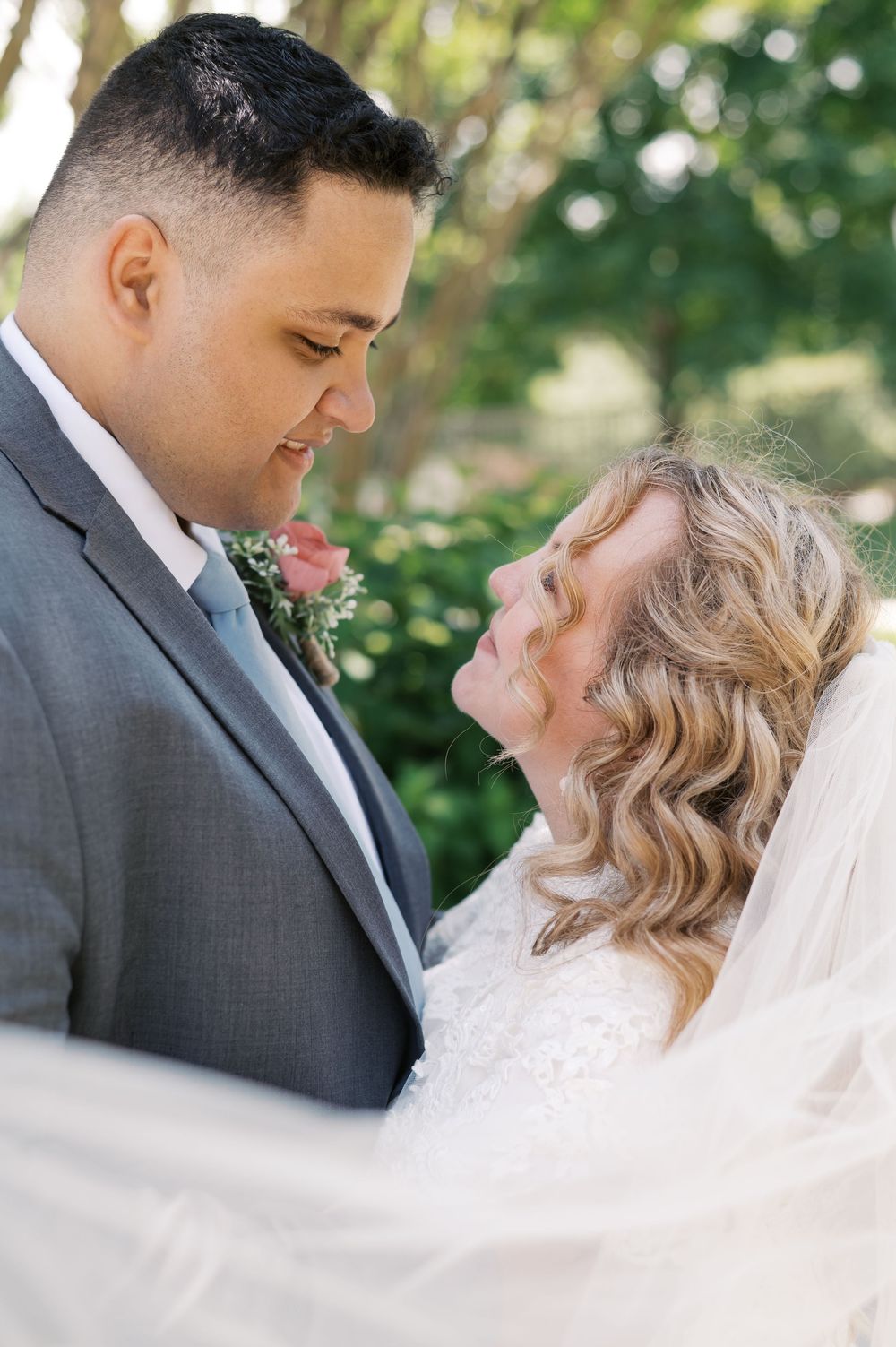 A romantic wedding portrait shows a couple in embrace outdoors with a sheer veil flowing in the foreground.