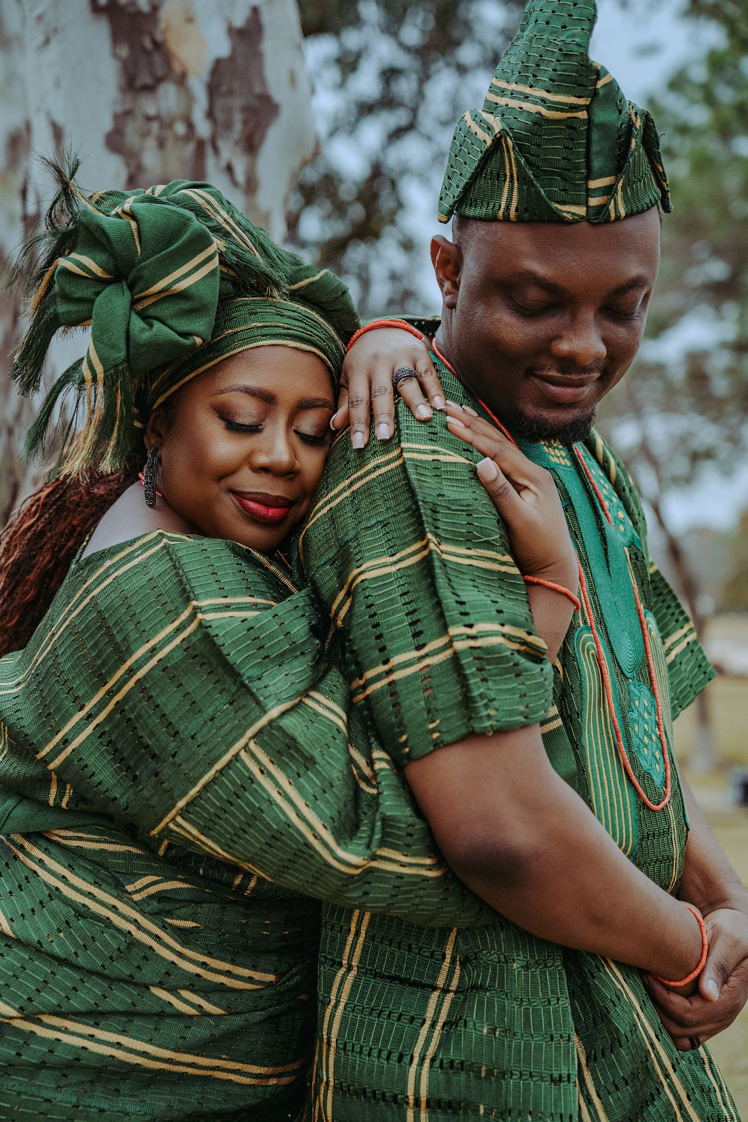 A couple wearing traditional Nigerian green and gold aso-oke attire embrace lovingly during a formal photoshoot.