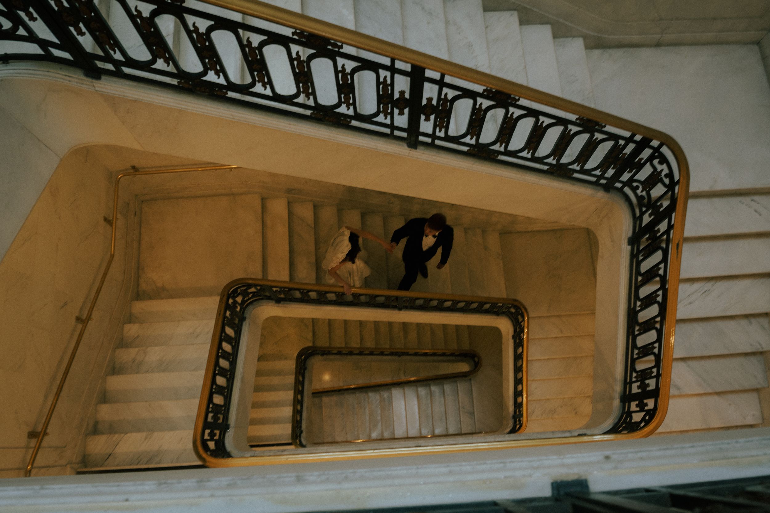 Decorative wrought iron handrails run along cream-colored walls in a curved stairwell with natural lighting.