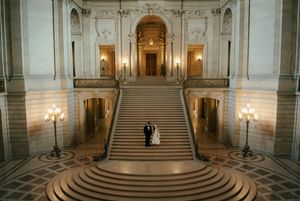 Interior panorama of San Francisco City Hall's grand staircase with ornate marble columns and illuminated wall sconces.
