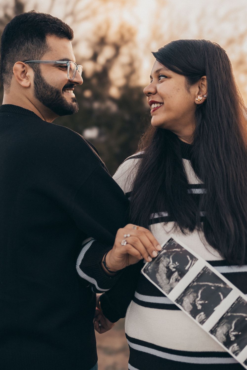 A couple shares a joyful moment while holding ultrasound photos outdoors.