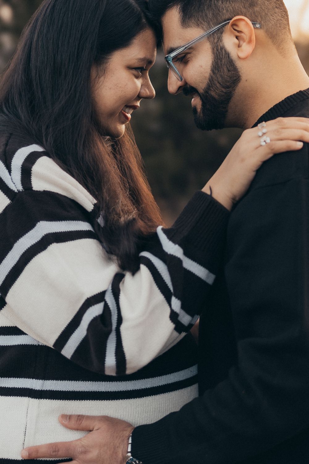 A couple embraces while wearing contrasting black and striped white sweaters outdoors.