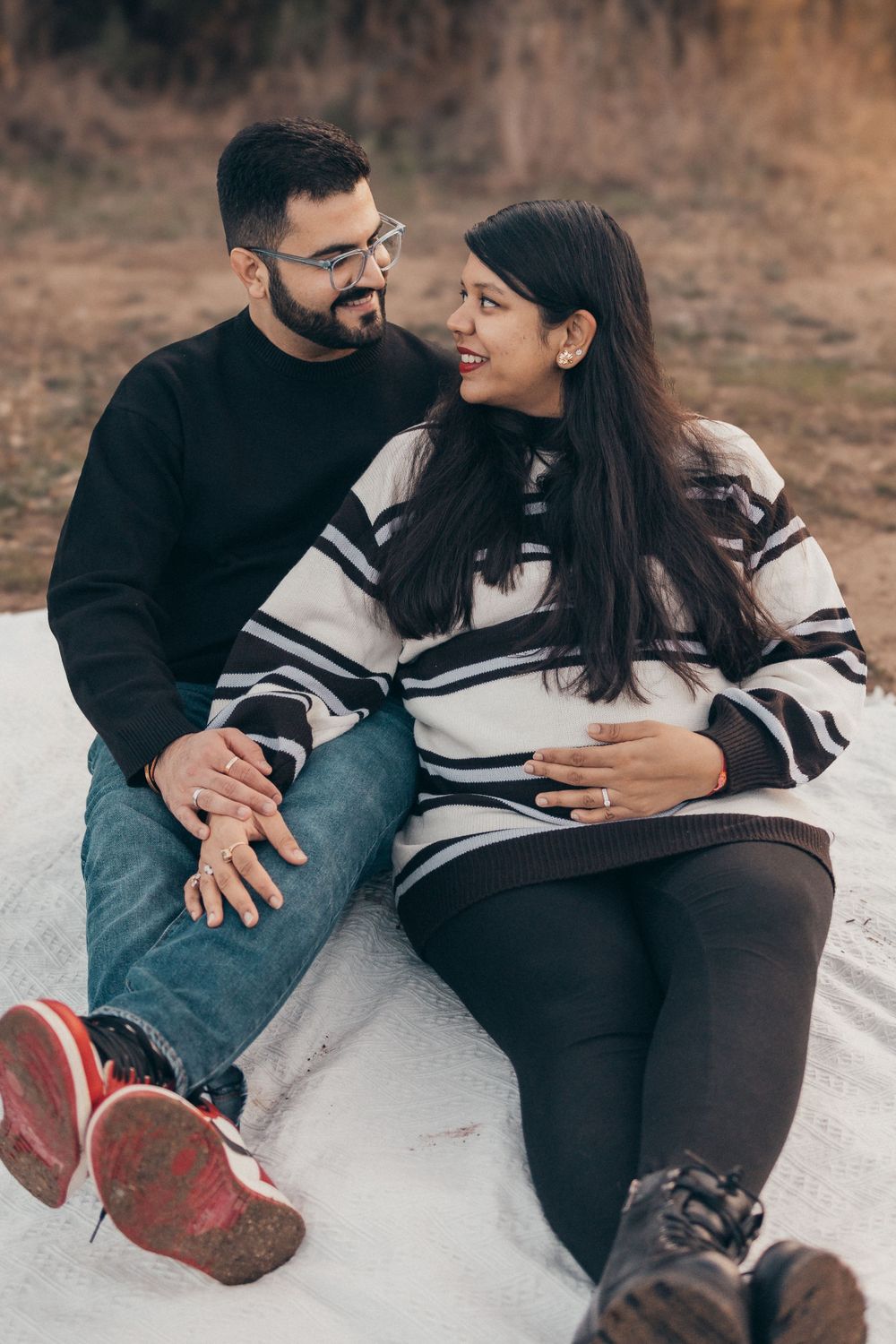 Couple shares intimate moment on blanket during outdoor pregnancy photoshoot.