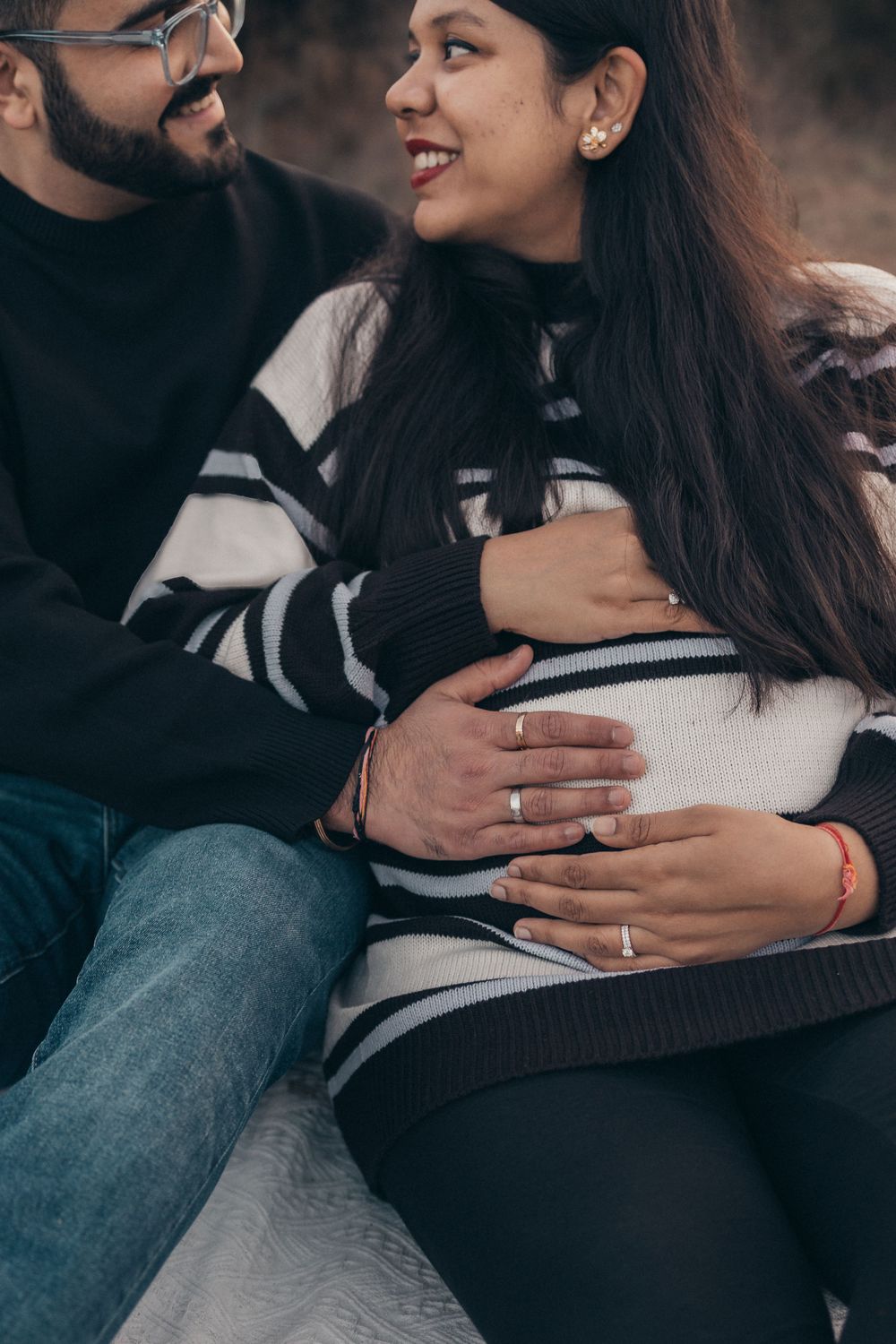 Intimate maternity moment captured as couple sits together on white blanket outdoors.