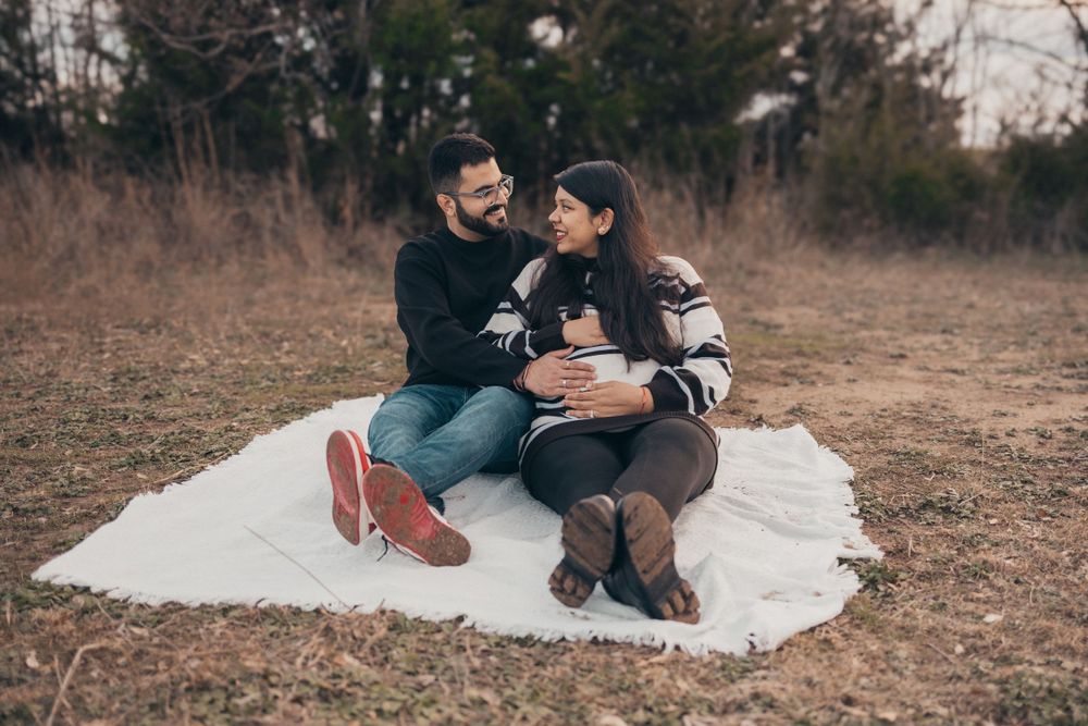 Couple sits together on white blanket during rustic outdoor maternity session.