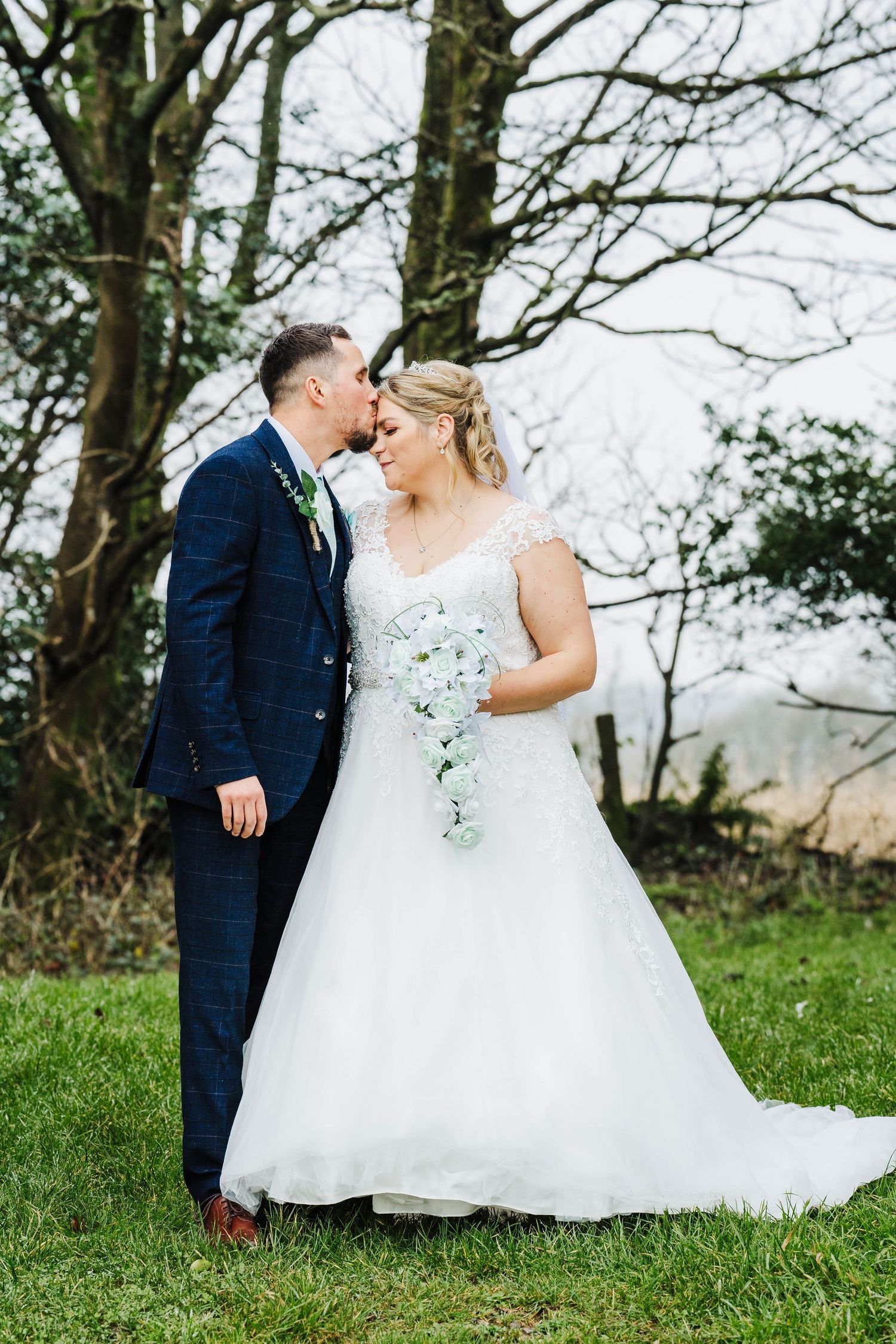 Romantic wedding portrait of couple embracing on green hillside surrounded by trees.
