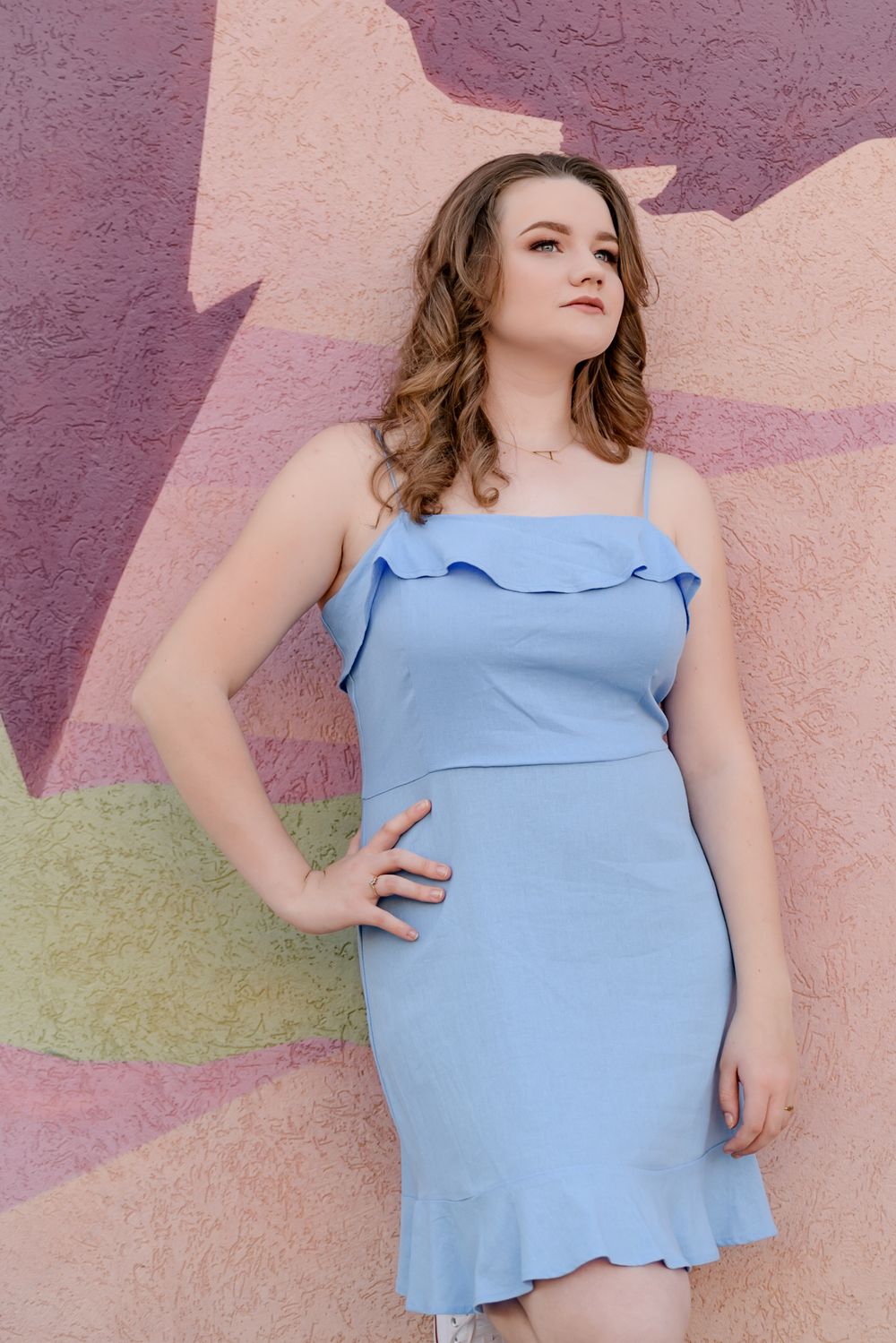 Portrait against colorful mural wall wearing light blue ruffle dress.