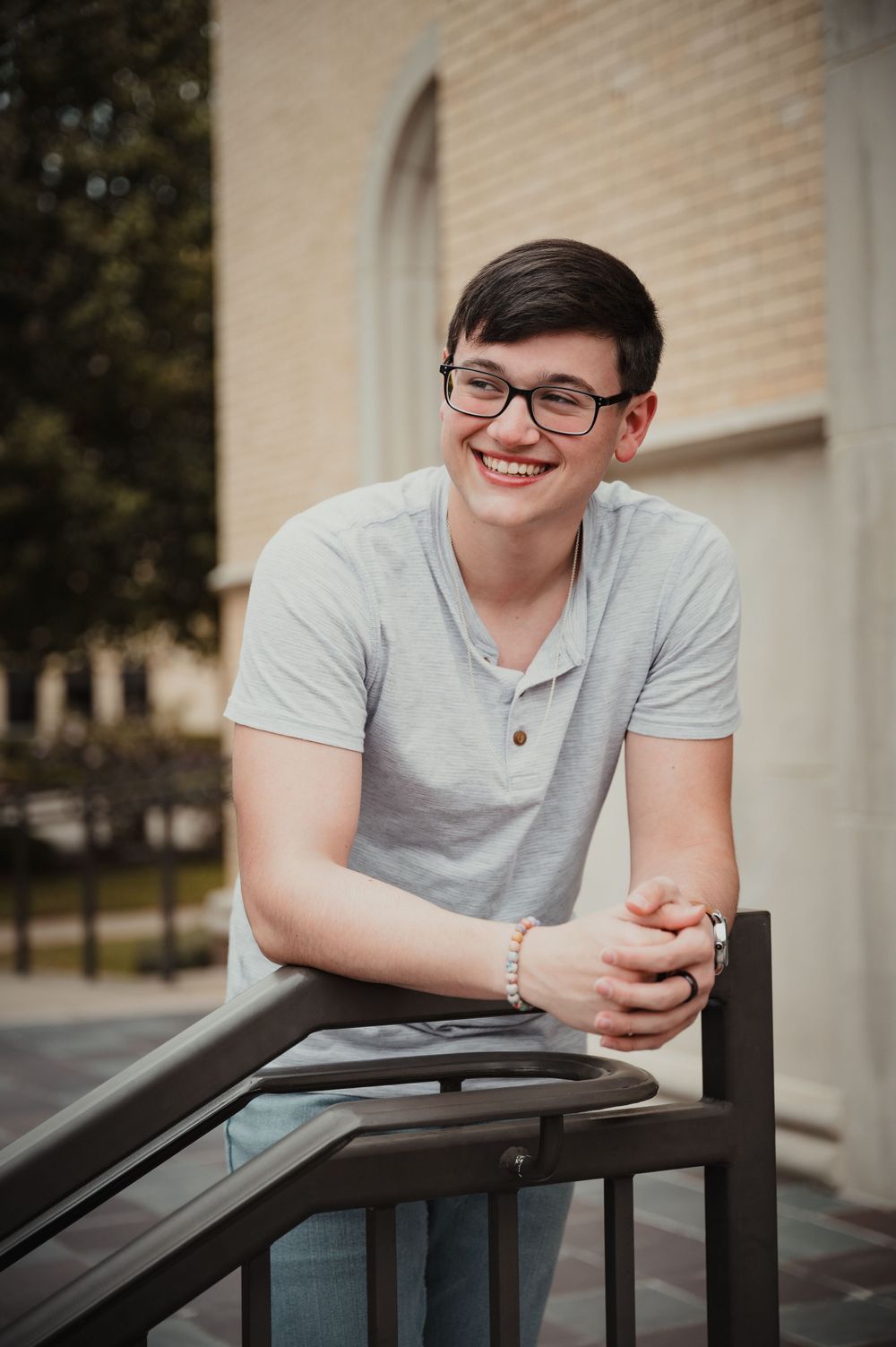 Person in gray shirt leans on railing while smiling at camera.