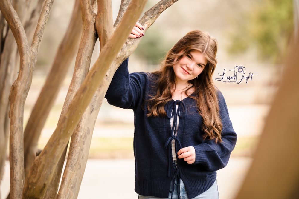 Someone posing by a tree branch wearing a navy blue sweater in natural lighting.