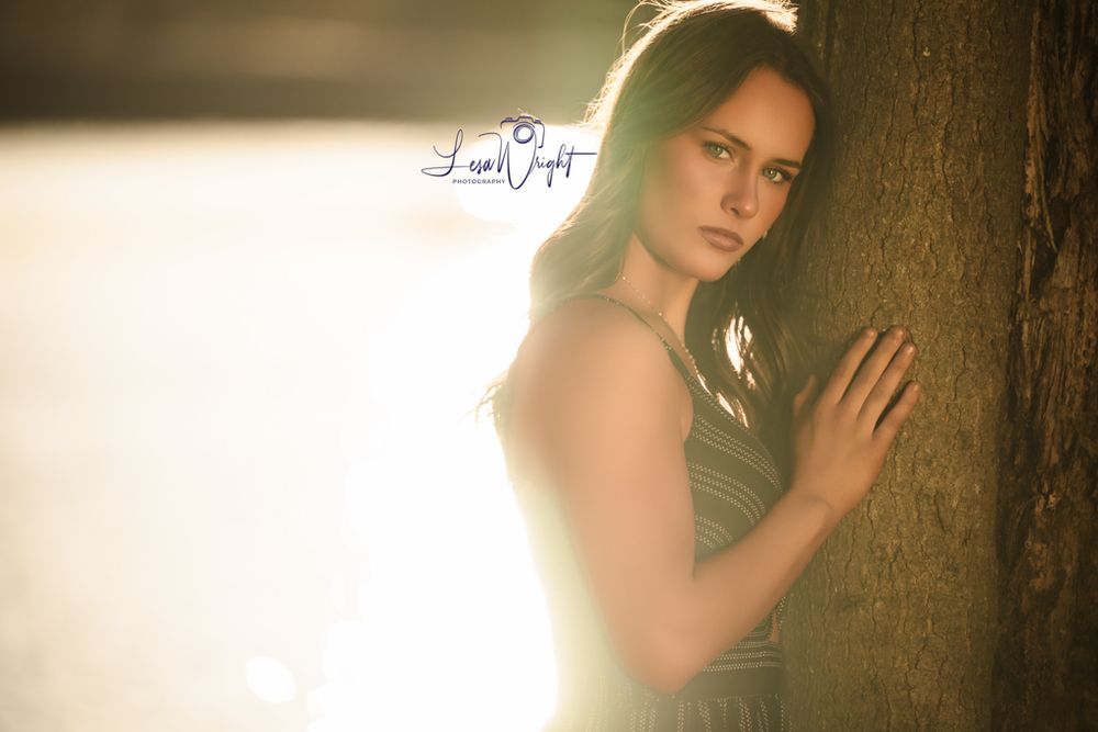 Artistic backlit portrait against a tree trunk with dramatic golden hour lighting.