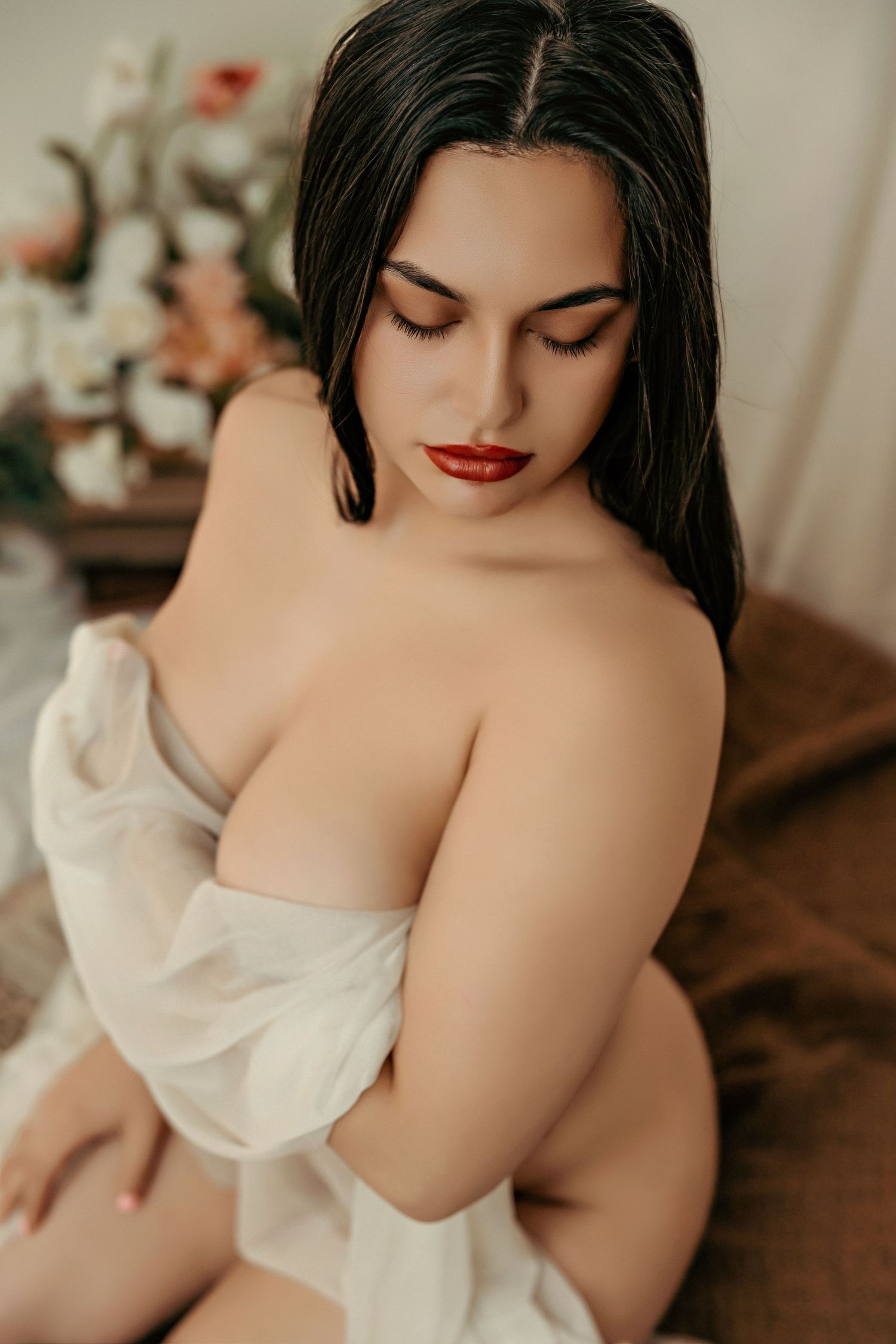 Model with dark hair poses softly draped in white fabric during intimate portrait session.