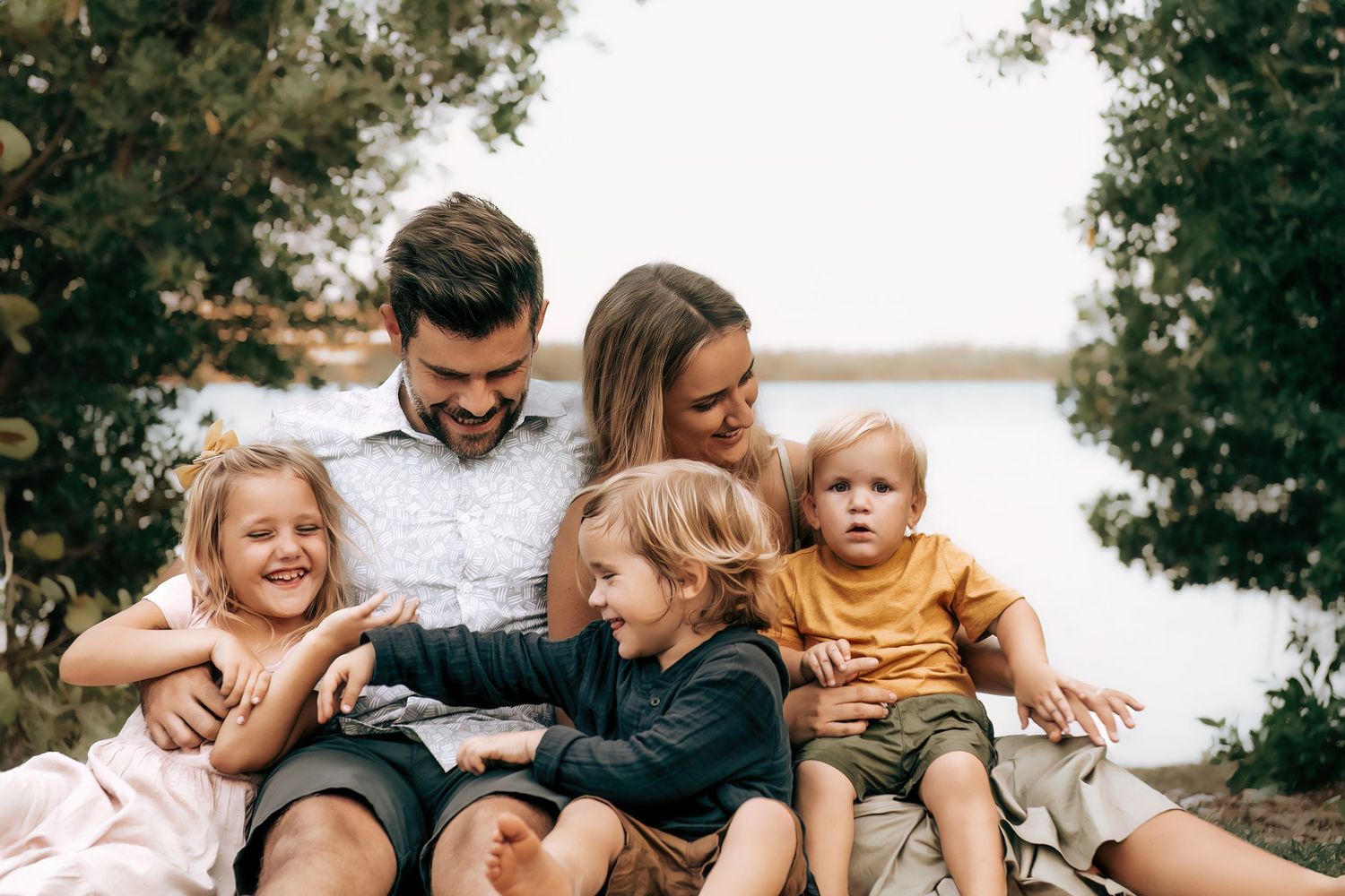 A candid moment of a family sitting together outdoors by a lake sharing laughter and joy.