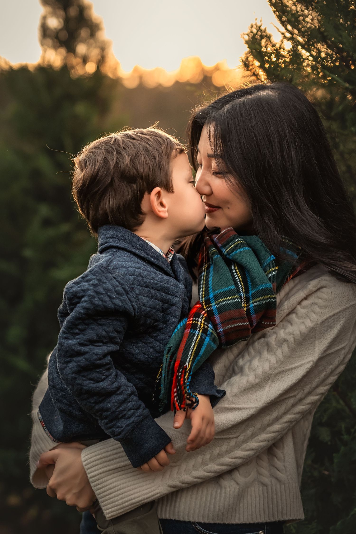 A tender moment between mother and son at Christmas tree farm with sunset in the background during golden hour.