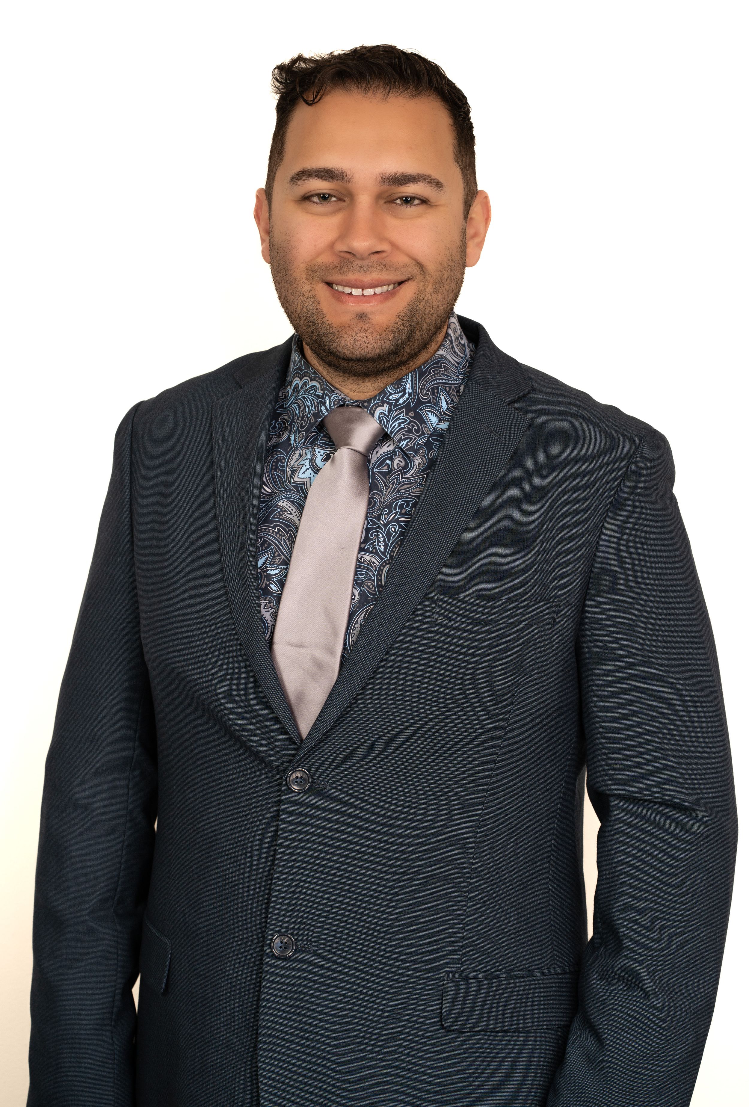Professional wearing a dark suit jacket with patterned tie and light shirt poses against white background.
