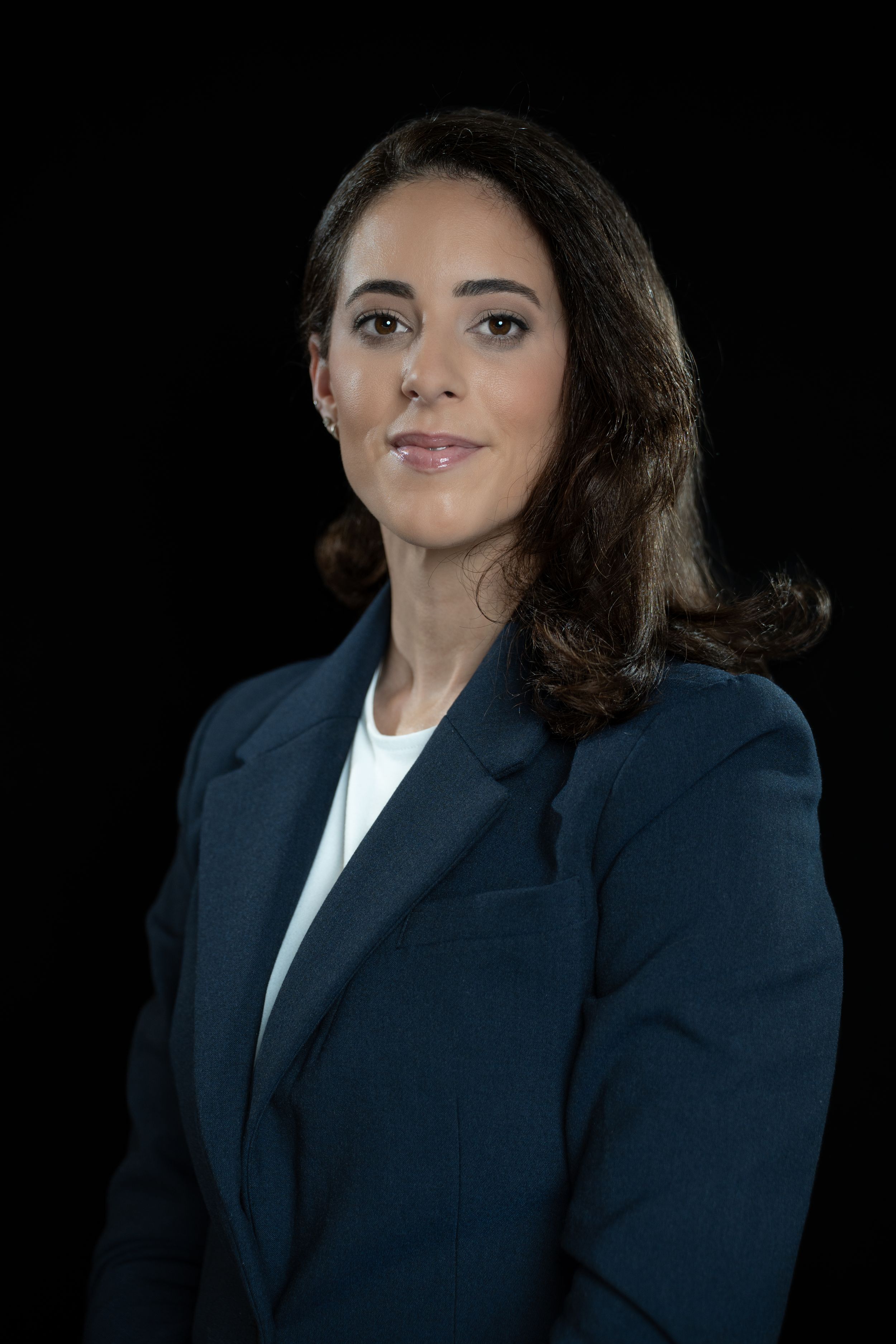 Professional headshot portrait in Tampa, Florida — confident woman wearing navy blazer and white top against dark background.