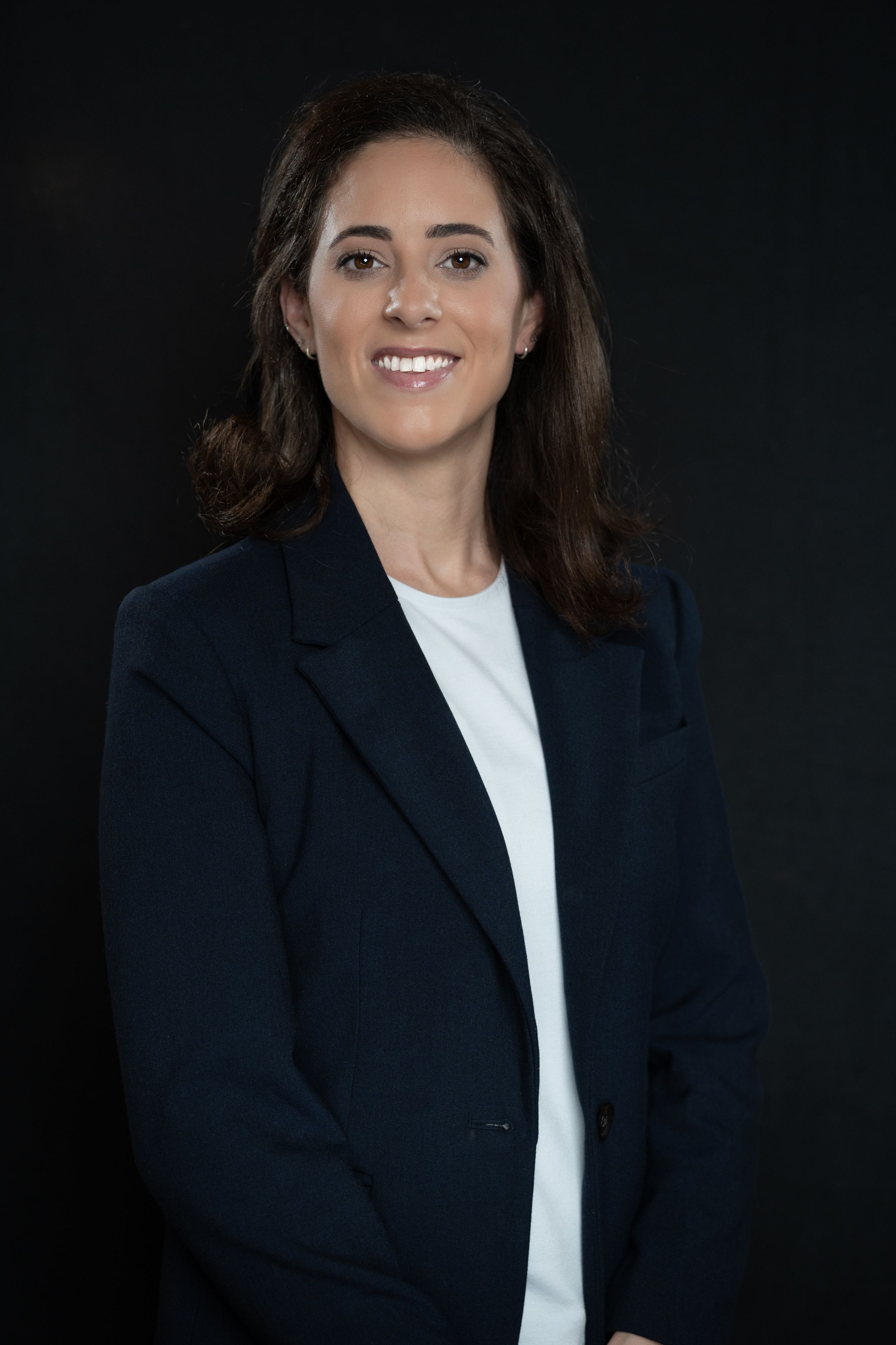 Professional headshot portrait on dark background — confident woman wearing navy blazer and white top, Tampa business photography.