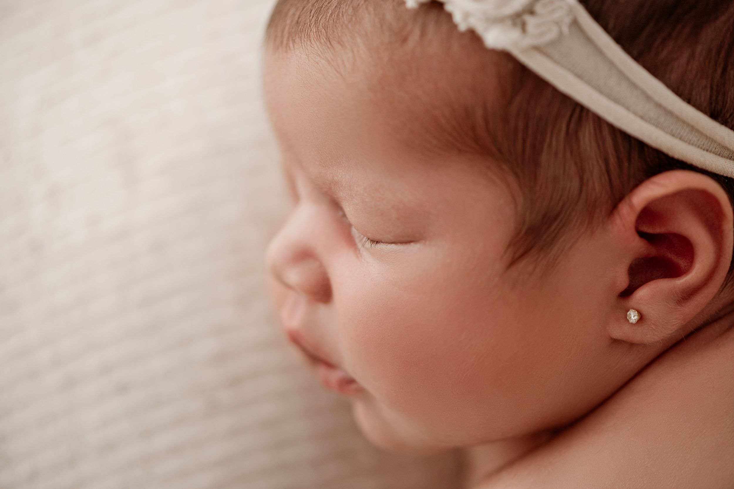 Close-up profile view of a sleeping infant wearing a delicate white headband and small earring.
