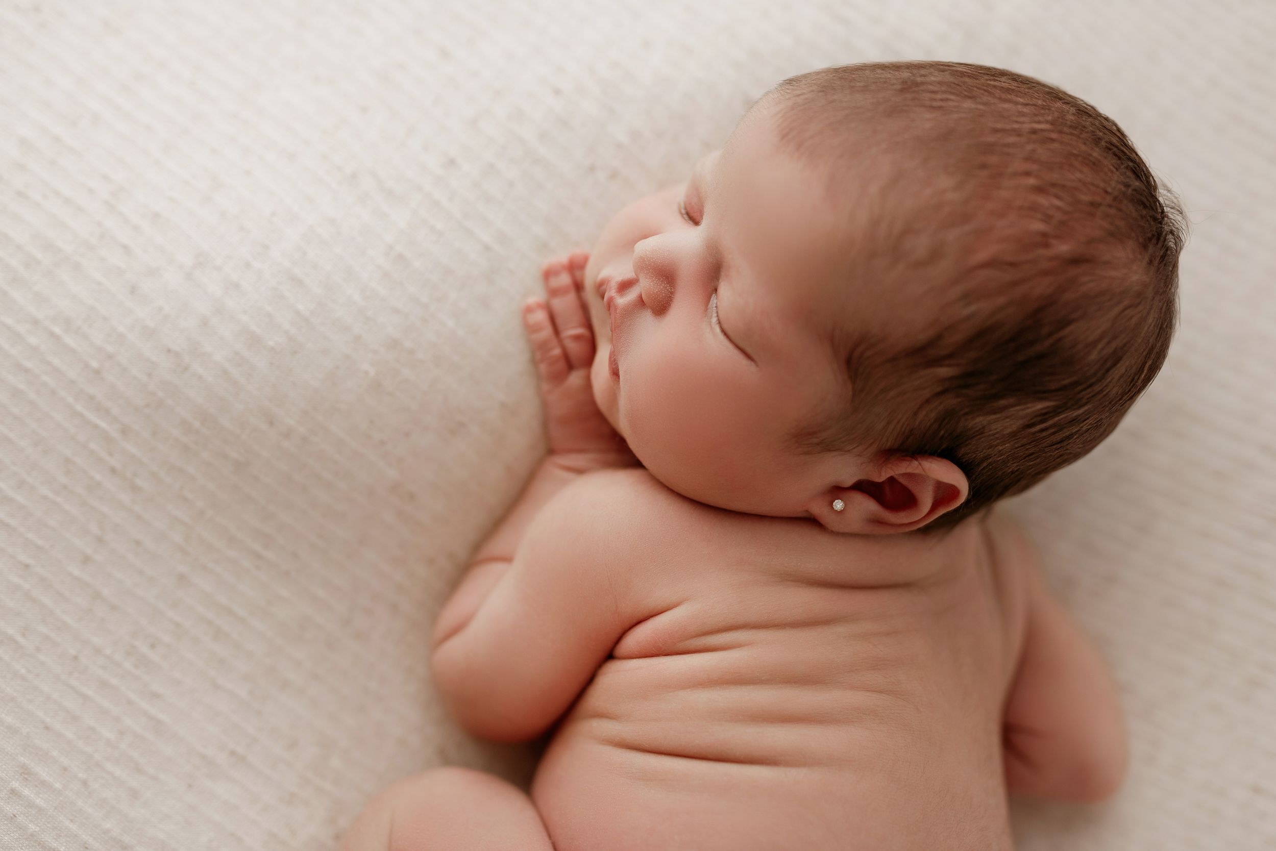 A peaceful sleeping newborn baby lies on a soft white blanket in a minimalist style portrait.