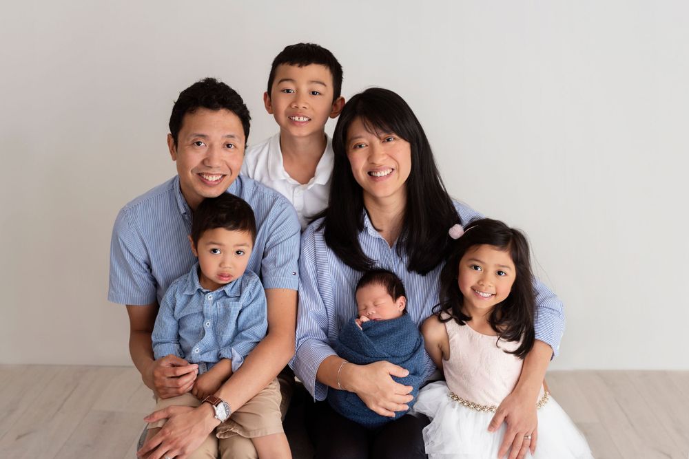 Family wearing matching blue shirts poses together on white floor during indoor photo session.