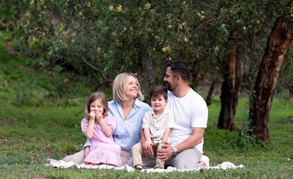 Family photo session on white blanket surrounded by natural greenery and trees.