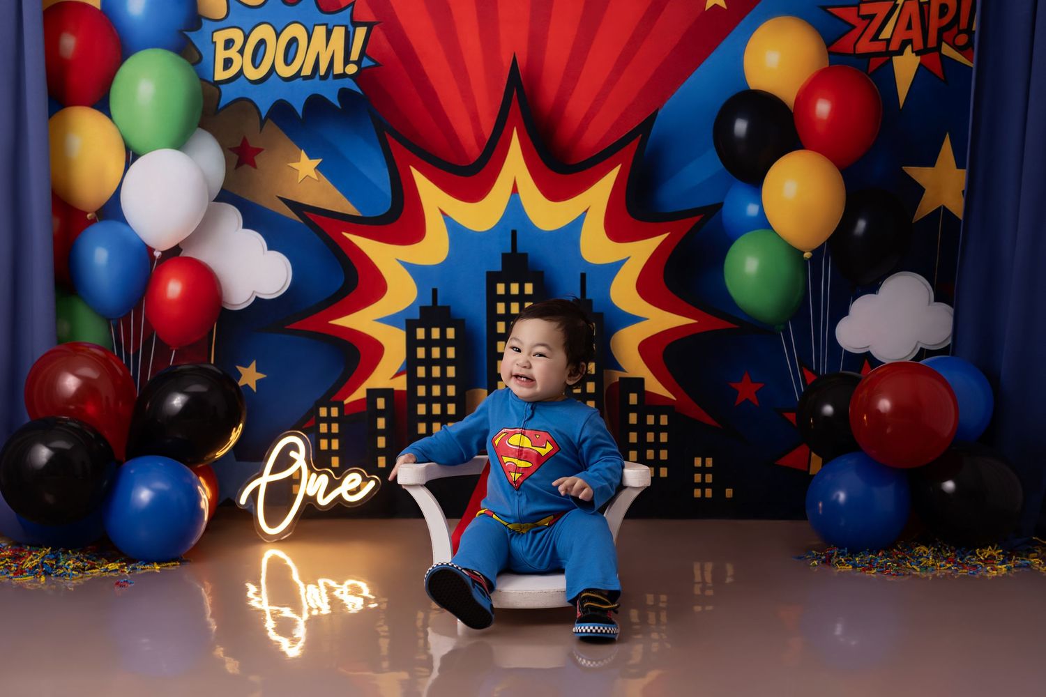 First birthday party setup with black and gold balloon arch, large black ONE letters, and stars against white backdrop.