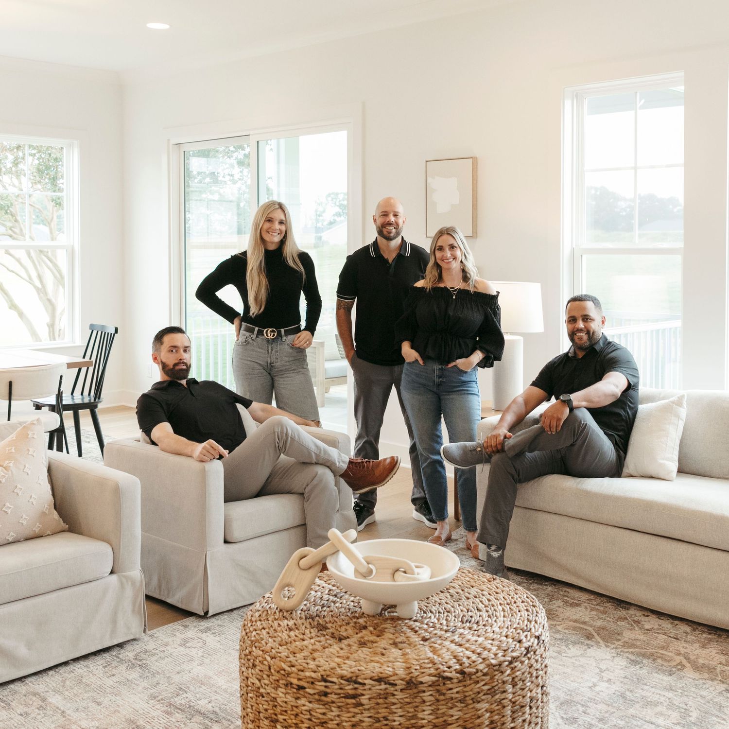 Group relaxing in modern living room with white sofas and woven ottoman centerpiece.