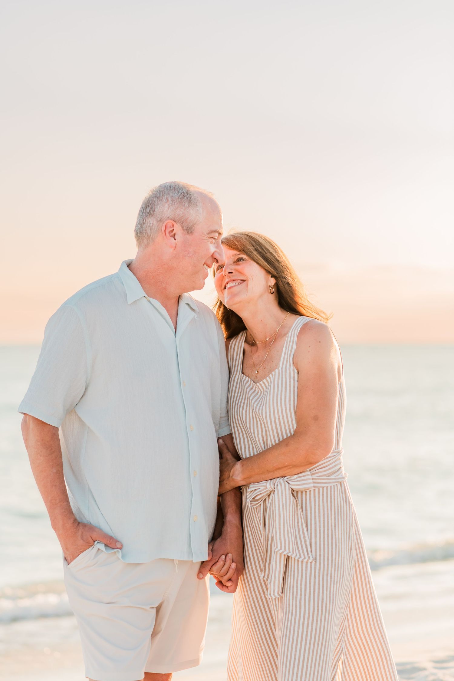 A loving couple shares a tender moment while walking hand in hand on a beach at sunset.