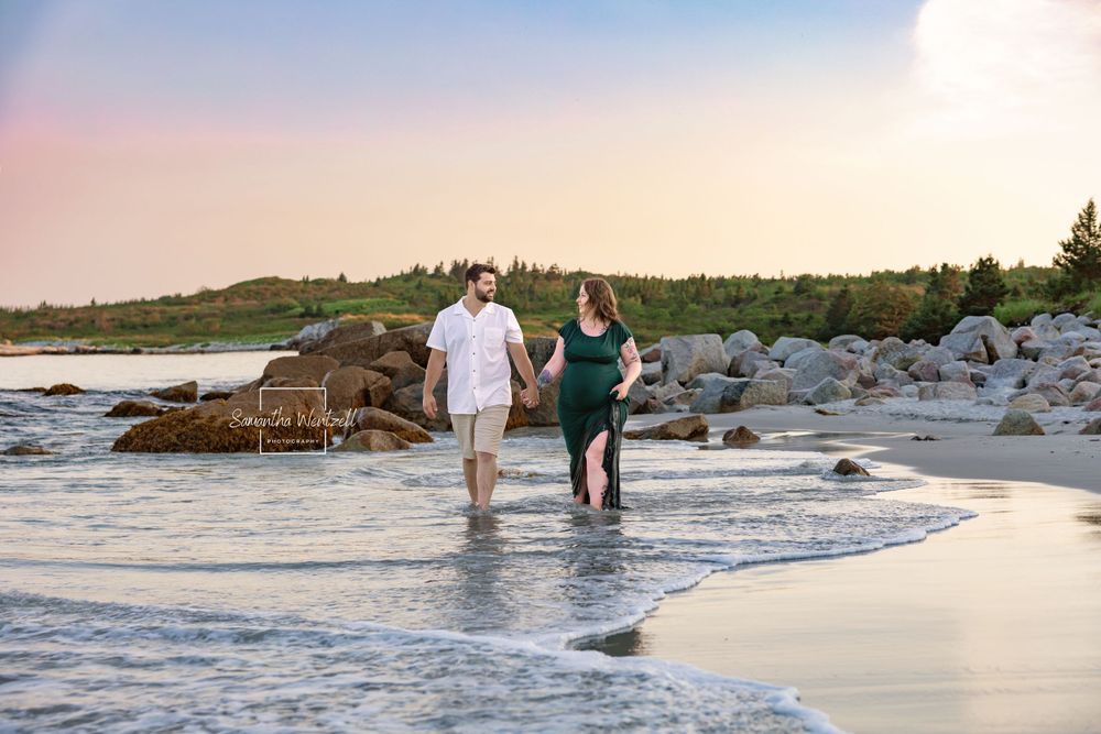Two people strolling together on a sandy beach at sunset with waves lapping at their feet. Maternity Photography, beach photography