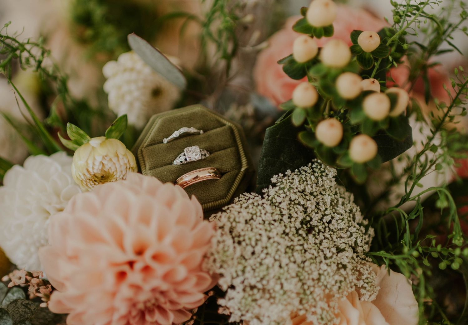 Wedding rings displayed in a velvet box among a lush floral arrangement of pink dahlias and white blooms.
