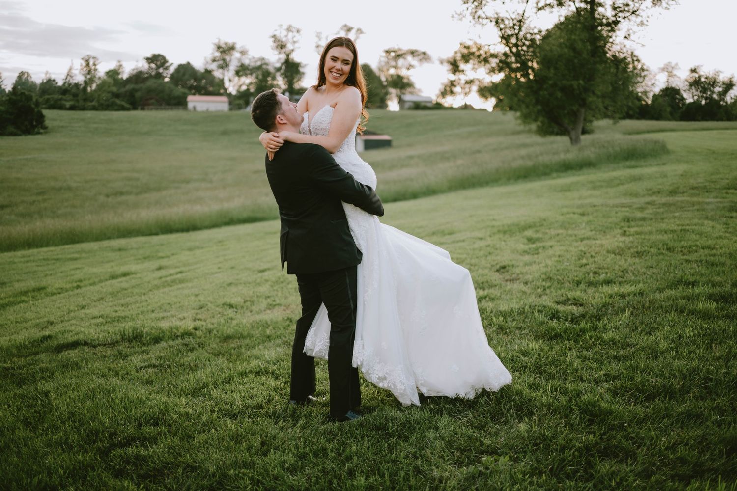 Wedding couple walking through a lush green field at sunset creating a romantic silhouette.