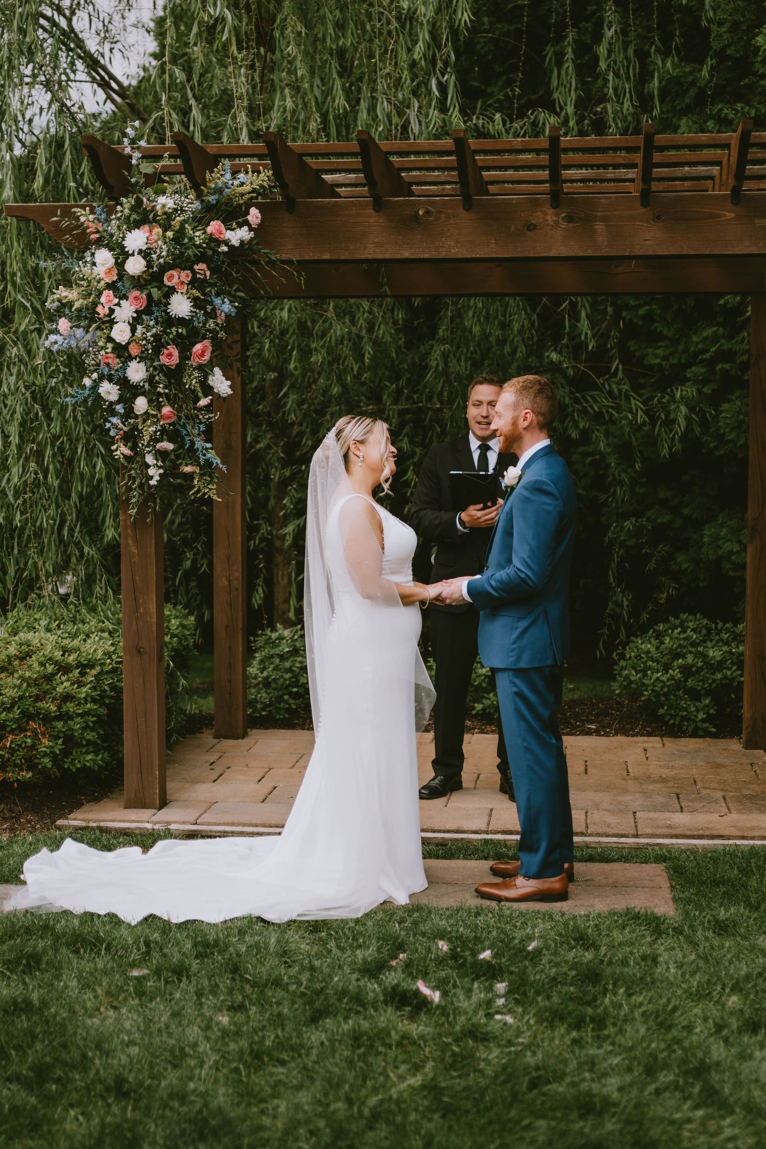Wedding ceremony first look under wooden pergola with weeping willow trees in background.