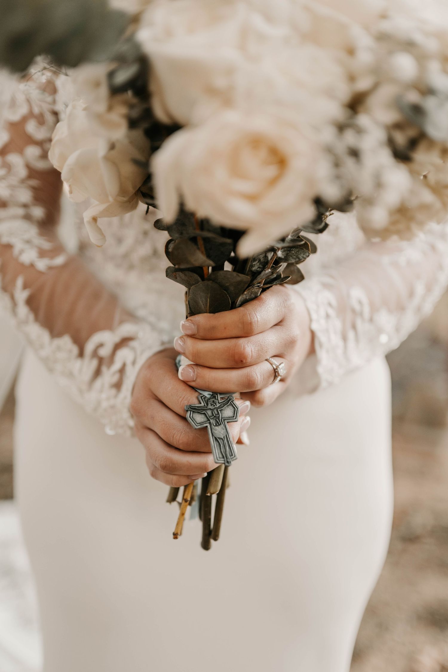 Close-up of hands holding a bridal bouquet with white roses and vintage details.