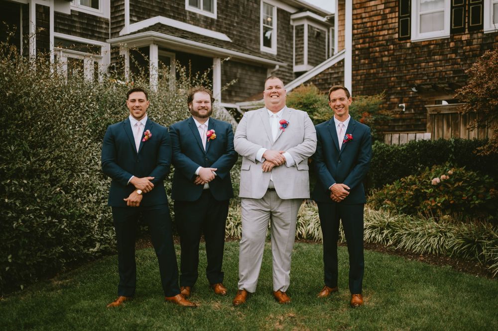 Wedding party members pose for formal photos on lawn in front of brick building.