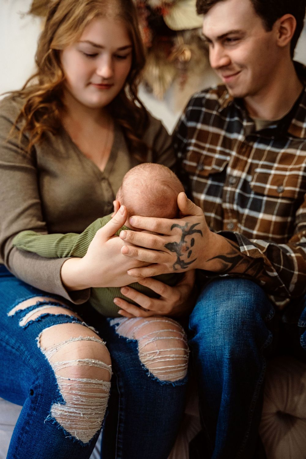 A couple in casual clothing holding a newborn baby together while sitting on a couch.