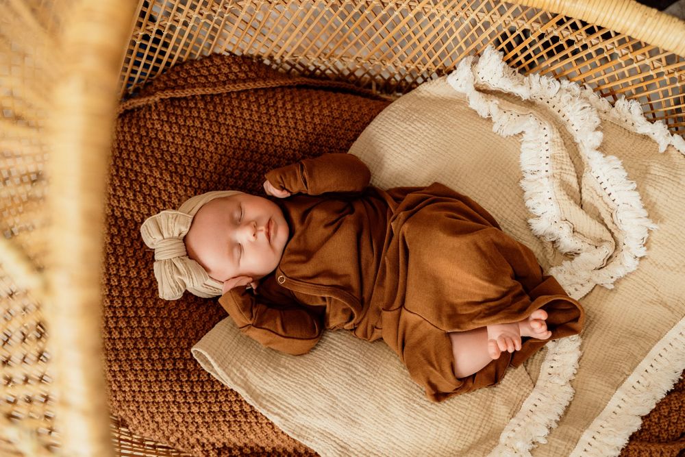 A sleeping figure rests peacefully on a woven rattan chair surrounded by soft white fabric and natural textures.