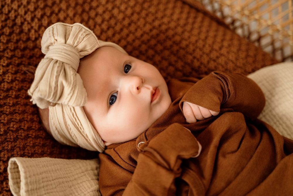 Seven sequential photos show a baby in a brown knit blanket looking towards the camera with changing expressions.
