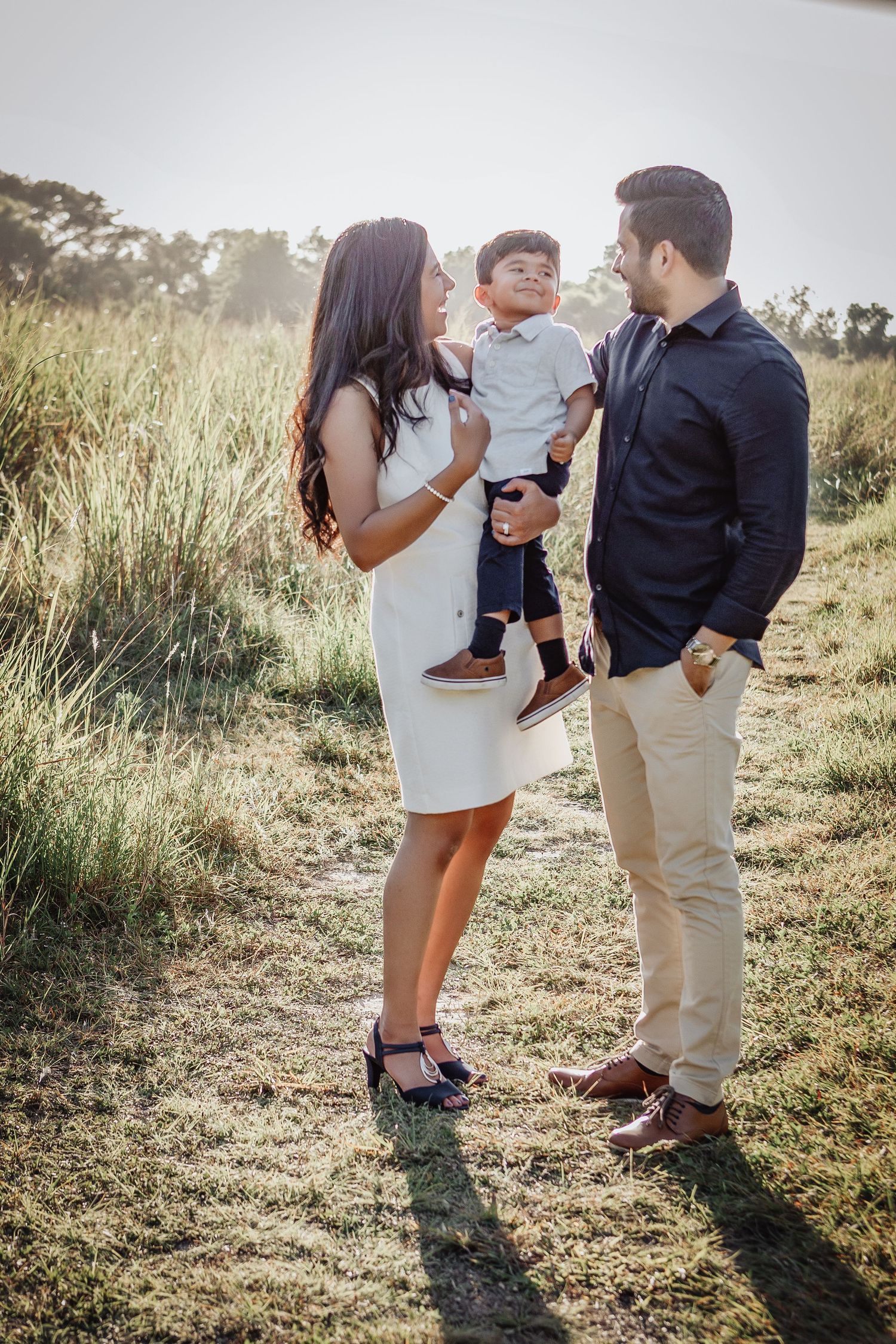 A loving family shares a tender moment together outdoors in a sunlit grassy field during golden hour.