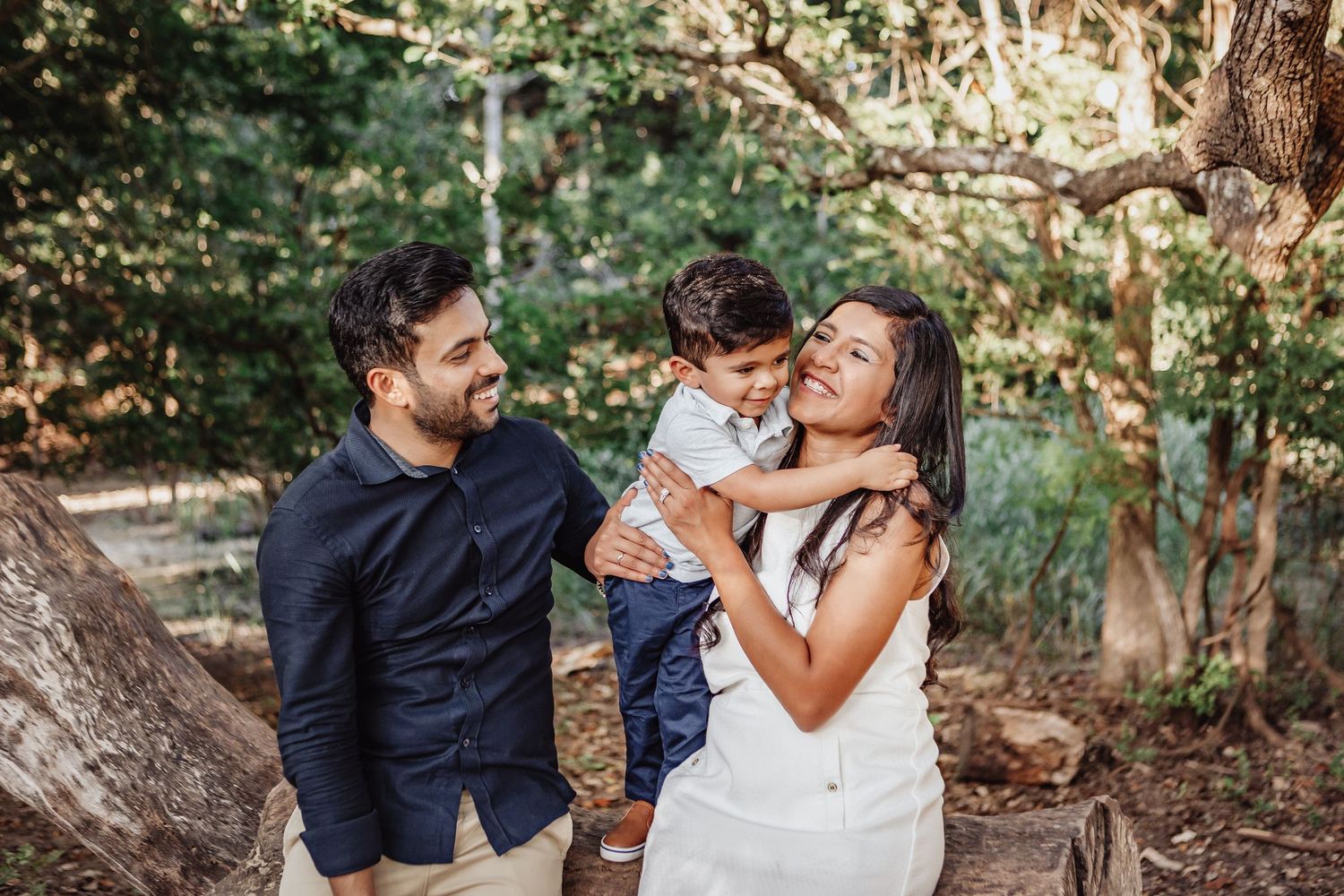 A happy family shares joyful moments together on a wooded path during a sunny outdoor photo session.