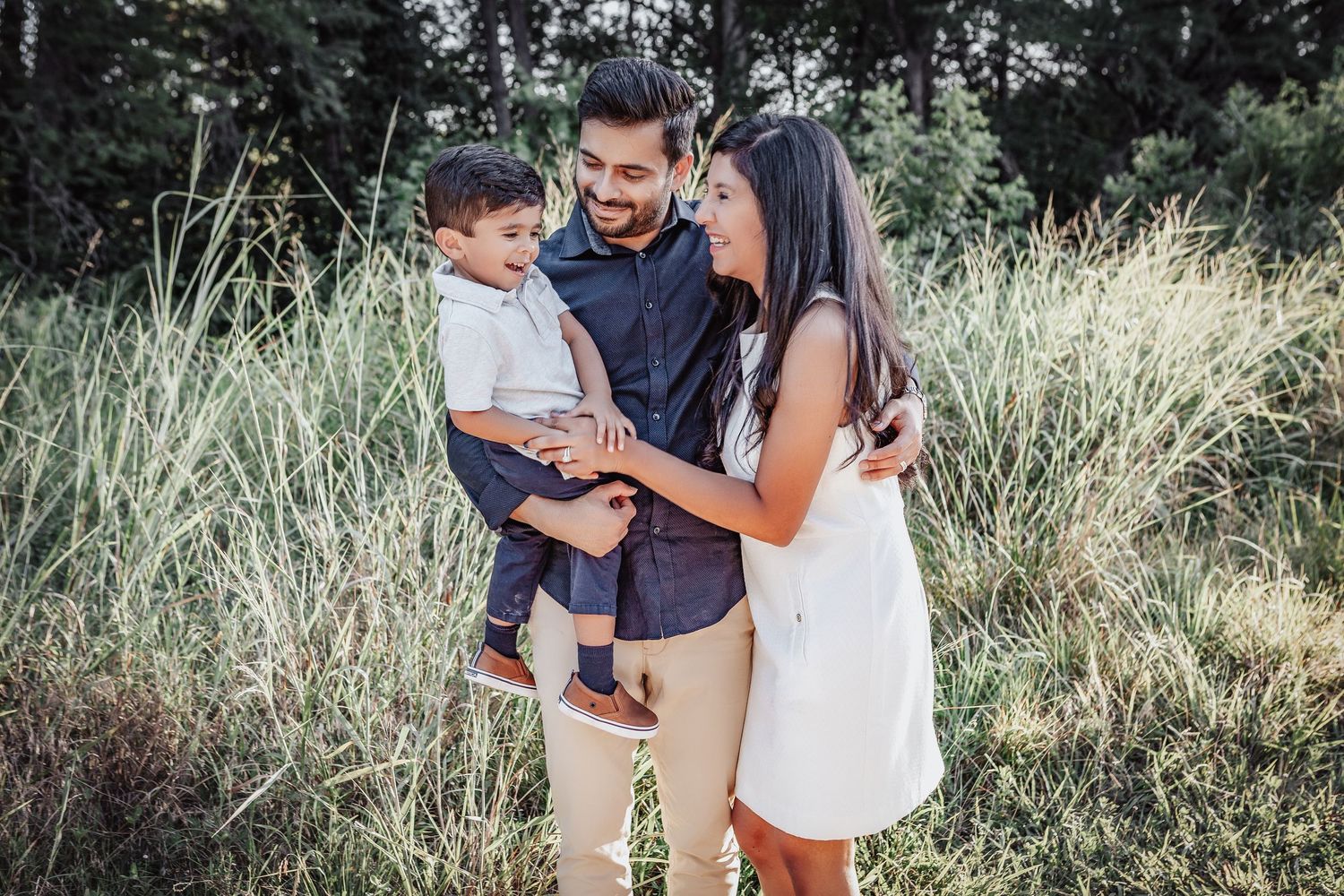 A family stands together in a grassy field on a sunny day wearing casual summer attire.