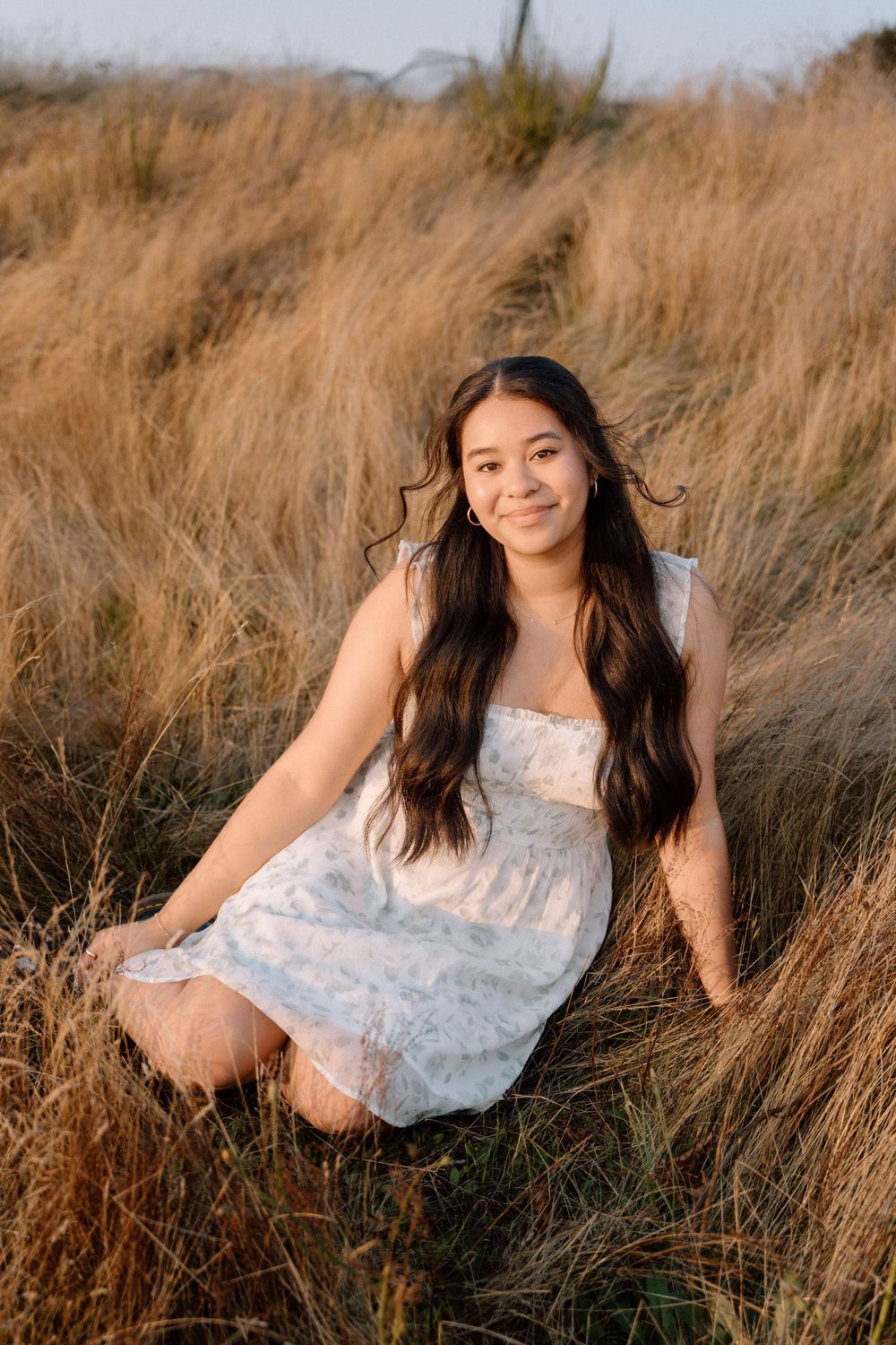 A person wearing a white dress poses in tall golden grass during golden hour.
