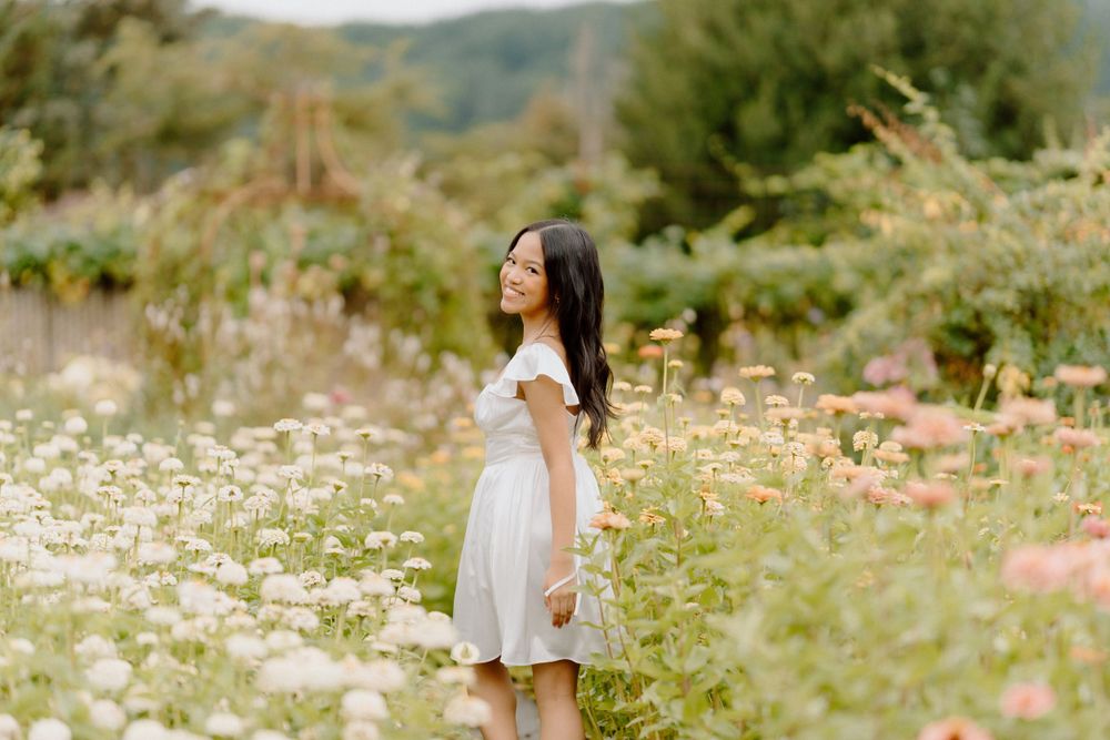 A person in a white dress stands among wildflowers in a dreamy garden setting.