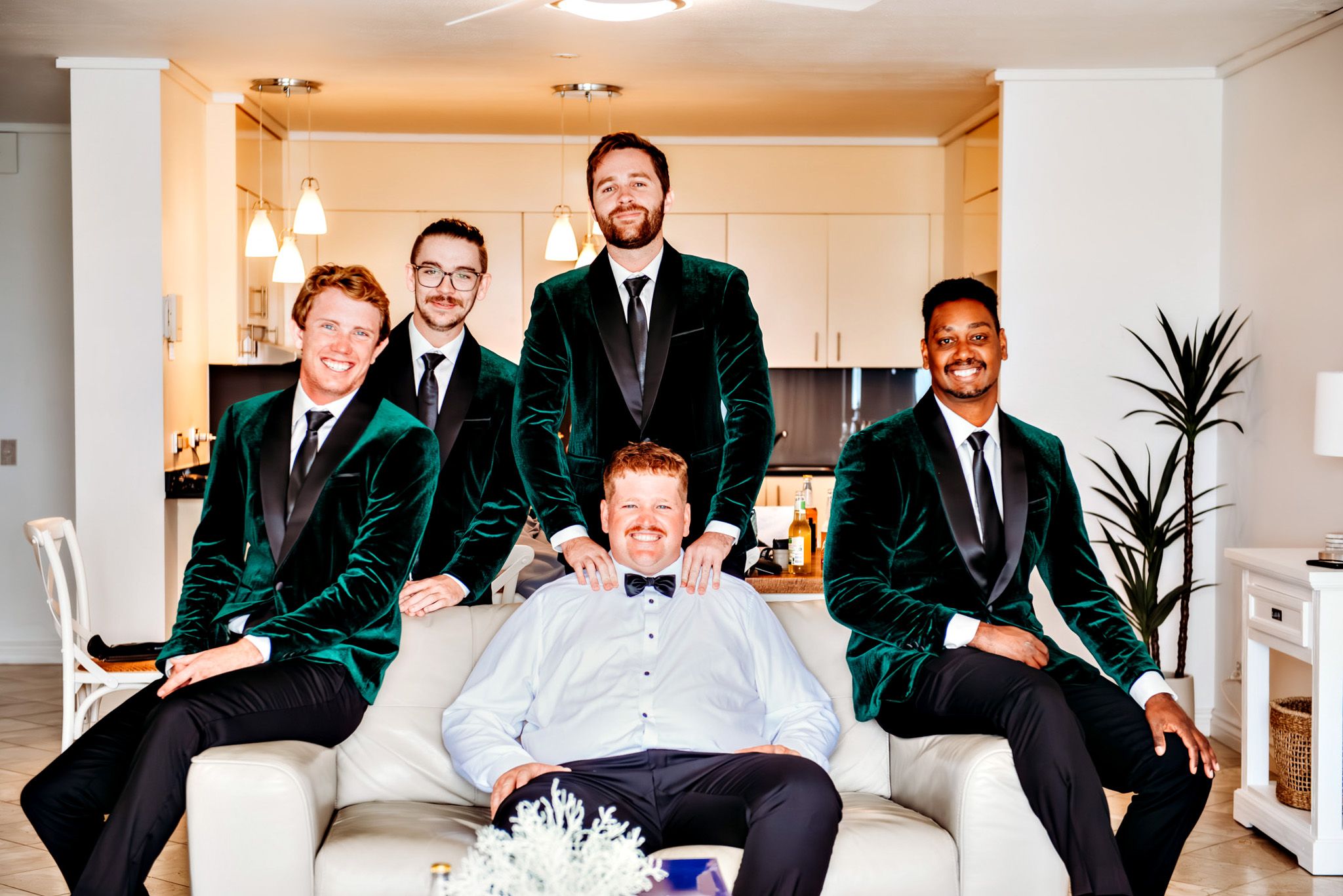 Groomsmen in emerald green velvet jackets pose together in an elegant indoor setting.