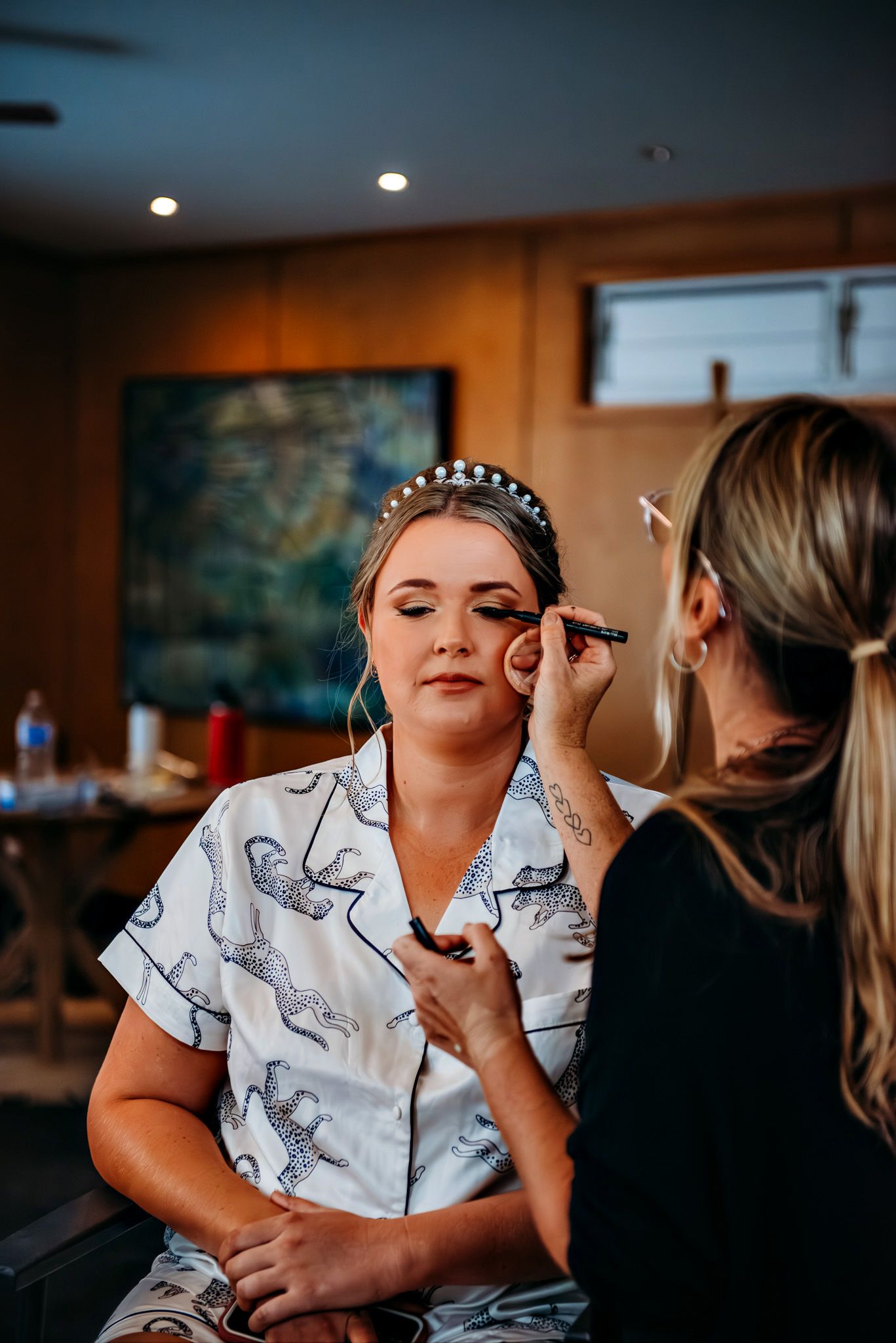 Makeup artist applies cosmetics to a person wearing a white robe during wedding preparations.