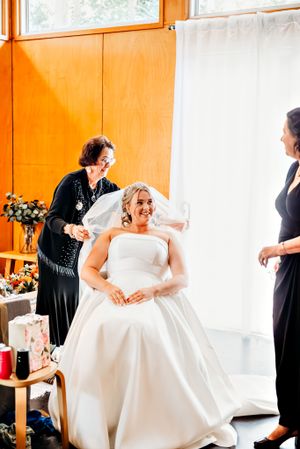 Wedding party helps with final dress preparations in a bright orange-walled room.