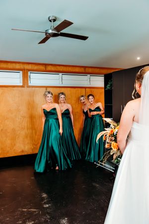 Wedding party in emerald green dresses gathered in a wood-paneled room.