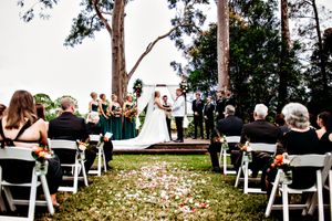 Outdoor wedding ceremony setup with white chairs and flower petals scattered along the aisle.