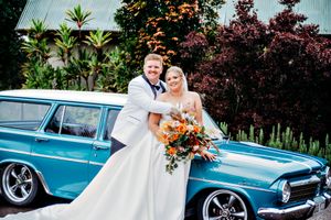 Classic blue vintage car serves as elegant wedding transportation against natural backdrop.