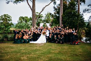 Large wedding group photo taken outdoors with guests arranged on grassy hillside.